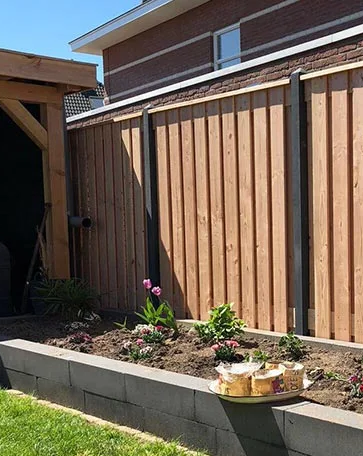 Betonschutting kleur antraciet met douglas tuinschermen en daarvoor een plantbak van zwarte stapelblokken