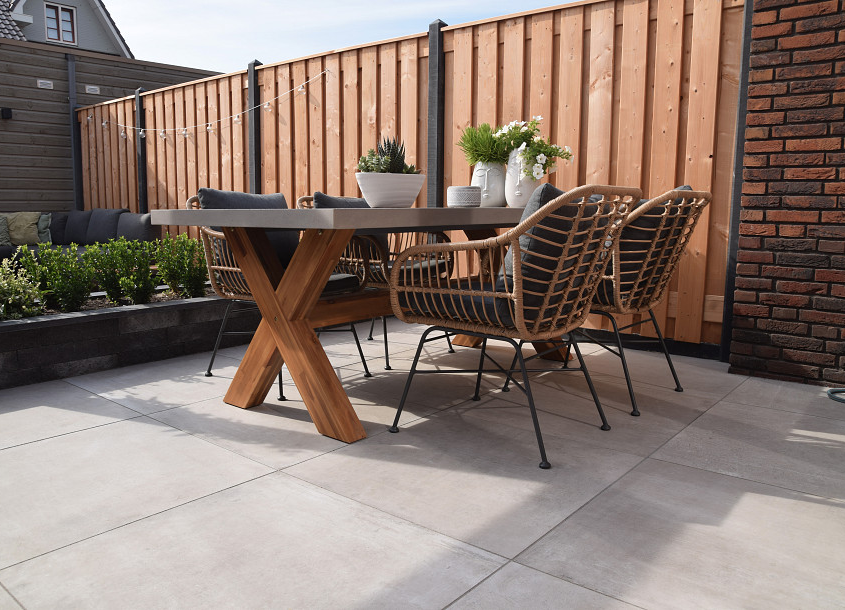 Bestrating van lichtgrijze terrastegels met daarop een eettafel en vier tuinstoelen